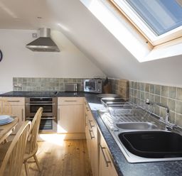 A kitchen with wooden dining table and chairs a stove sink and skylight window at 4 Armada House in Hope Cove