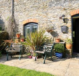 A stone wall with two benches and potted plants near a black door at Cowslip Cottage in Frogmore