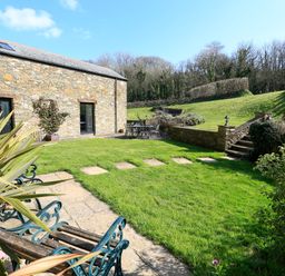 A stone building with a black door and window beside a grassy garden with chairs and a table at Cowslip Cottage in Frogmore