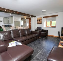 A living room with brown leather sofas a wood stove and an open kitchen at Cowslip Cottage in Frogmore