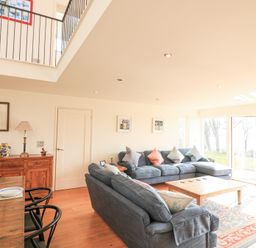 A living room with blue sofas a wooden coffee table and a dining table with chairs near large glass doors at Sea Peep in Thurlestone