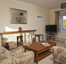 A living room with floral patterned sofas a wooden coffee table fireplace and a TV on a stand at Amberley in Dartmouth