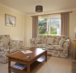 A living room with patterned sofas a wooden coffee table and a window with garden view at Amberley in Dartmouth