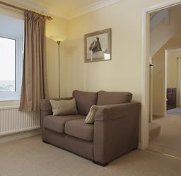 A living room with a brown sofa and floor lamp next to a window and dining room visible through a doorway at Amberley Dartmouth