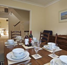 A dining table set with plates bowls glasses and bottles in a dining room with wooden chairs at Amberley in Dartmouth