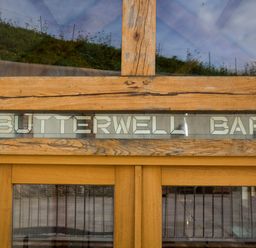 A wooden door with glass panels and a stained glass sign above reading Butterwell Barn at Butterwell Barn in Dartmouth