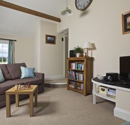 A living room with a sofa with pillows a small table with a chess set a wooden bookshelf and a TV on a white stand at Cloverwell in Woodleigh