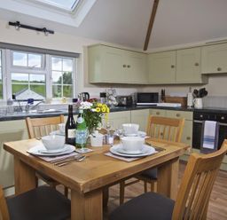 A kitchen with a wooden dining table set for four with dishes and flowers at Cloverwell in Woodleigh