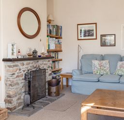 A living room with a stone fireplace sofa with floral cushions wooden coffee table and bookshelves at Cottage View in Hope Cove