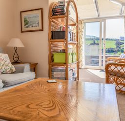 A living room with a coffee table sofa armchairs bookshelf and sliding glass doors at Cottage View in Hope Cove