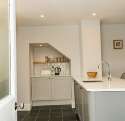A kitchen with a white countertop island sink kettle toaster and wooden bowl at Cindys Retreat in Hope Cove