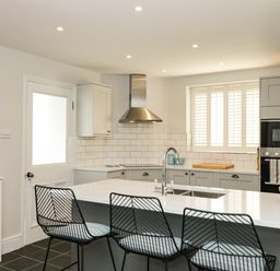 A kitchen with three black wire bar stools at an island with a sink and white countertop at Cindy's Retreat in Hope Cove
