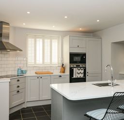 A kitchen with gray cabinets white countertop and a window with shutters at Cindy's Retreat in Hope Cove