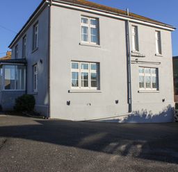 The exterior of a two-story house with white walls and multiple windows next to a paved driveway at Cindy's Retreat in Hope Cove