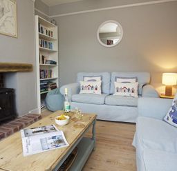 A living room with light blue sofas a wooden coffee table a bookshelf and a wood burning stove at Crab Cottage in Salcombe