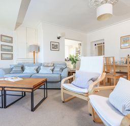 A living room with a blue sofa white armchairs wooden coffee tables a dining table and chairs at Edinburgh House in Salcombe