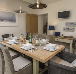 A dining room with a wooden table set with plates glasses and bottles surrounded by six wicker chairs at Gooder House in Dartmouth