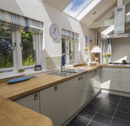 A kitchen with wooden countertops white cabinets a sink a stove and windows with striped blinds at Gooder House in Dartmouth