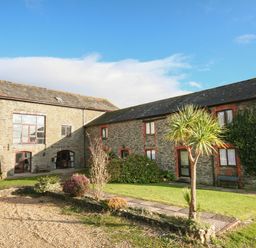 An outdoor view of two stone buildings with small windows surrounded by grass and plants at The Granary Malborough