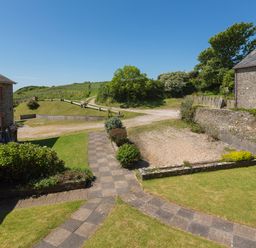 A stone pathway leading to grassy areas and two stone buildings under a clear blue sky at The Granary Malborough