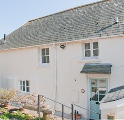 Exterior view of a white cottage with blue door and windows with shutters at Hazel Cottage in Malborough