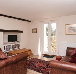 A living room with two brown leather sofas a wooden coffee table a patterned rug and a television on a shelf at Hazel Cottage in Malborough