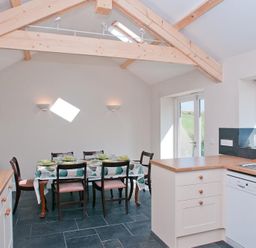 A kitchen with wooden countertops a dining table with chairs and crockery under wooden ceiling beams at Hazel Cottage in Malborough