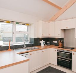 A kitchen with white cabinets wooden countertops a double sink an electric stove a kettle and kitchen utensils at Hazel Cottage in Malborough