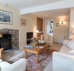 A living room with a stone fireplace a wooden coffee table flowers and cream sofas at Jot Cottage in Salcombe