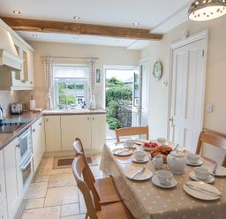 A kitchen with a dining table set for tea and an open door leading to a garden at Jot Cottage in Salcombe