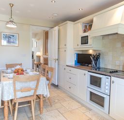 A kitchen with a dining table set for breakfast and white cabinets with appliances at Jot Cottage in Salcombe