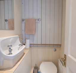 A small bathroom with a wall-mounted sink a mirror a towel on a rack and a toilet at Jot Cottage in Salcombe