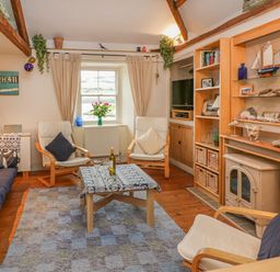 A living room with wooden beams two armchairs a wooden coffee table a window and built in shelves at Lee Shore in Salcombe