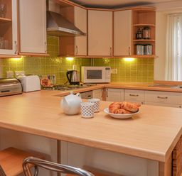 A kitchen with wooden countertop and cabinets a teapot cups and pastries on the counter at Lee Shore in Salcombe