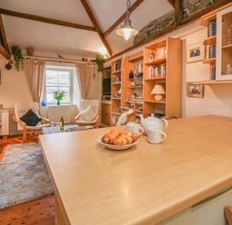 A living room with chairs a wooden table and shelves with books and decor at Lee Shore in Salcombe