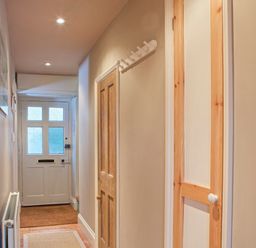 A hallway with a white front door wooden doors coat hooks and a radiator at Lee Shore in Salcombe