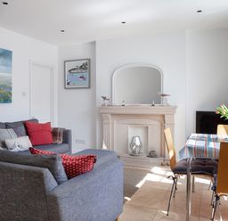 A living room with blue sofas red cushions a fireplace and a dining table with flowers at Lower Fernlea in Salcombe