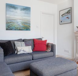 A living room with blue sofas and cushions a painting above the sofa and a fireplace at Lower Fernlea in Salcombe