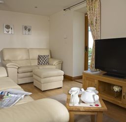 A living room with cream leather sofas a wooden TV stand with a television and a small wooden table with a tea set at Meadow View in Modbury