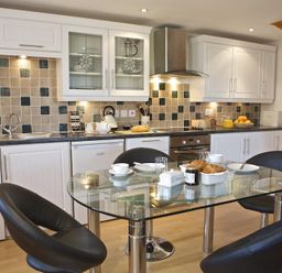 A kitchen with white cabinets dishwasher oven and a glass dining table with black chairs at Meadow View in Modbury