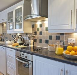 A kitchen with white cabinets tiled backsplash and countertop with oranges and a jug of orange juice at Meadow View in Modbury