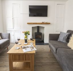 A living room with two grey sofas a wooden coffee table with wine glasses and a bottle and a wall mounted television at The Old Wash House in Dartmouth