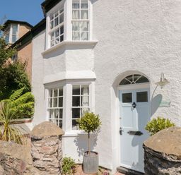 The exterior of a white house with a pale blue door and bay windows at The Old Wash House in Dartmouth