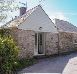 A stone cottage with a white door and a bush beside it at Orchard Barn in Salcombe