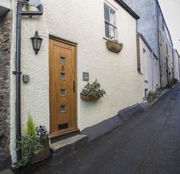 A narrow street with a wooden door numbered 5 and flower pots on the walls at Pixie Cottage in Dartmouth