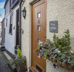A wooden door with the number 5 and a sign saying Pixie Cottage with flowers in a planter on a street in Dartmouth