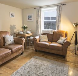 A living room with two brown leather sofas a wooden floor and a dining table at Pixie Cottage in Dartmouth