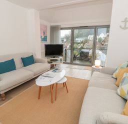 A living room with two sofas a coffee table a television and glass doors leading to a balcony at Prospects in Salcombe