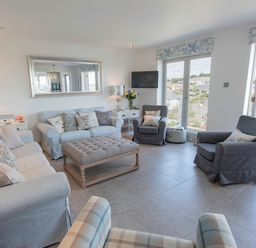 A living room with sofas armchairs a large ottoman and a wall mirror at Raleigh House in Salcombe