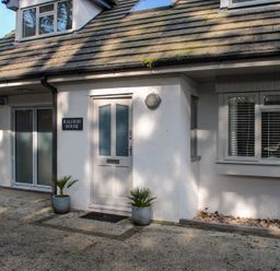 The outside entrance of a house with a door labeled Raleigh House and two plants in pots at Raleigh House in Salcombe